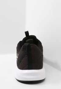 Svart vadderad träningsskor med vit gummisula, med en dragflik vid hälen och en vadderad krage för extra komfort.