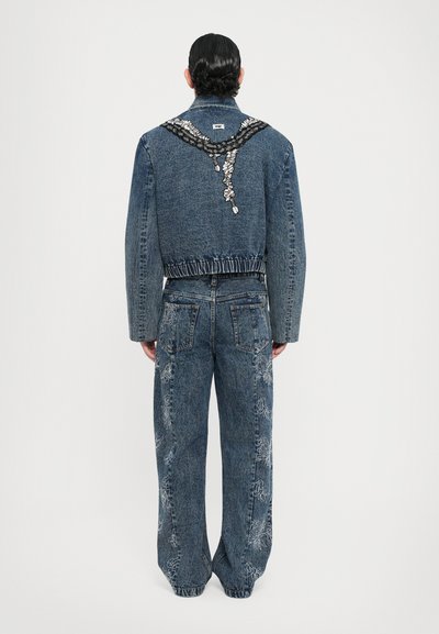 Denim jakk, mille seljaosas on lilleline tikand, elastne vöökoht, koos laia säärega denim pükstega, mille külgedel on tikitud kujundid.