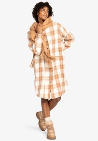 Rutet skjortekjole i creme og orange, knaplukning foran, lange ærmer, knælang. Sammen med et tekstureret beige tørklæde og brune støvler.