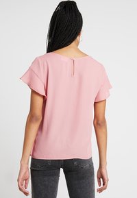 Blusa rosa a maniche corte realizzata in tessuto morbido. Presenta una chiusura a occhio di bue sul retro e maniche con volant. Design semplice, texture leggera.