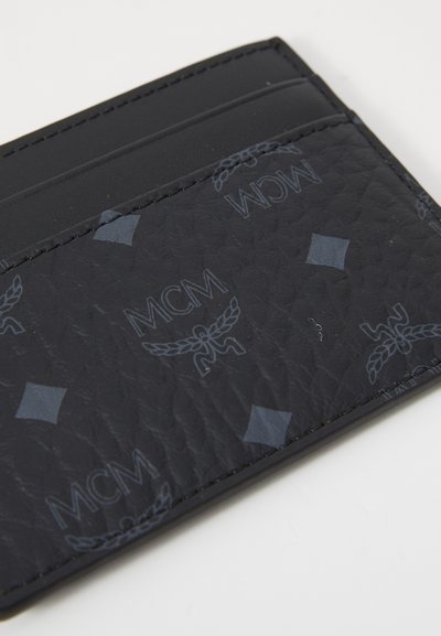 Svart lær kortholder med preget MCM-logo og geometriske mønstre. Slim design med fem kortlommer og strukturert overflate.