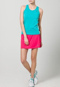 Top de tirantes turquesa con escote redondo, combinado con una falda deportiva rosa. Presenta un tejido transpirable y un logo de tres rayas en el lateral.