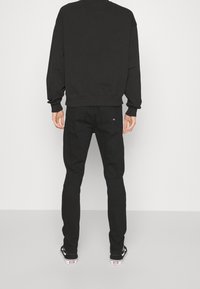 Černá mikina s kulatým výstřihem, dlouhými rukávy a žebrovanými manžetami, kombinovaná s černými slim-fit džíny. Tenisky mají černobílé provedení.