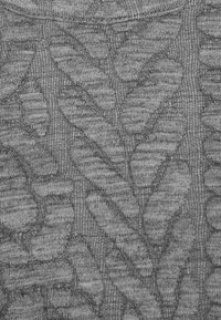 Tissu tricoté gris avec des motifs de feuilles en relief et texturés créant un design botanique détaillé.