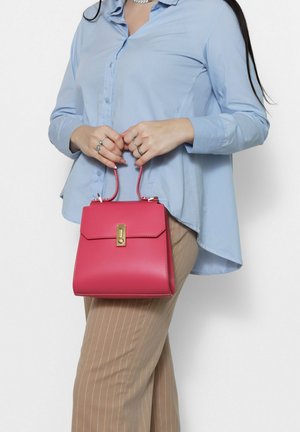 Borsa a tracolla in pelle rosa con un design strutturato, dettagli in hardware dorato e manico superiore. Abbinata a una camicia button-up azzurro chiaro e pantaloni a righe.
