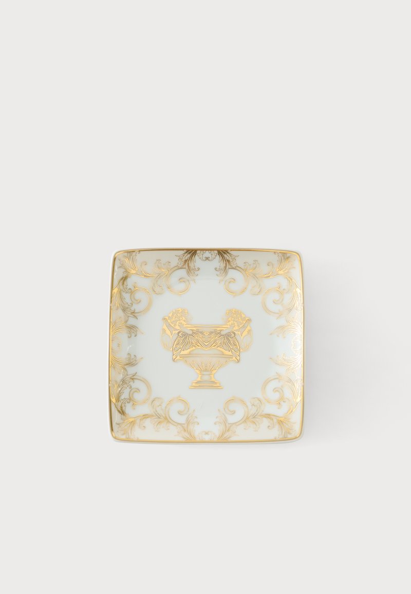 Assiette carrée en porcelaine blanche avec des volutes florales dorées ornées et un motif d’urne classique au centre.