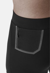 I pantaloni sportivi neri presentano una tasca testurizzata con chiusura a zip, accentuata da un bordo riflettente. Tessuto liscio con vita aderente.