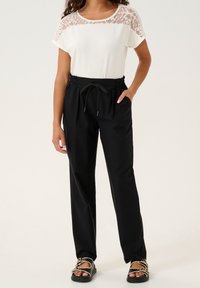 Svart, lättviktiga byxor med elastisk midja som kombineras med en vit topp med spetsdetaljer på axlarna. Avslappnad passform med dragsko.
