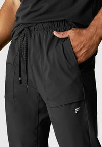 Schwarze Sporthosen verfügen über einen elastischen Bund mit Kordelzug, seitliche Taschen und ein elegantes Design mit dezentem Logo-Detail am Unterschenkel.