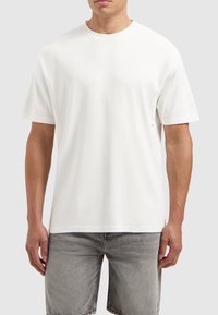 Witte katoenen t-shirt met een ronde halslijn en korte mouwen. Heeft een ontspannen pasvorm en een subtiele logo-detail aan de onderkant.