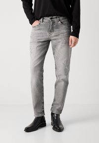 Jeans grii cu croi drept, cu textură estompată, ușor deteriorați la buzunare, asortați cu botine negre din piele la gleznă.