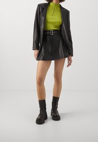 Černá mini sukně z umělé kůže a odpovídající sako v kombinaci s ribbovaným, krátkým rukávem limetkově zeleným topem. Celý outfit doplňují černé kotníkové boty.