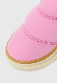 Primer plano de la punta de un zapato de tela rosa con costura texturizada y una suela de goma beige con un patrón de zigzag.