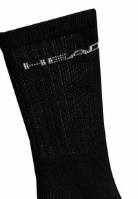 Chaussette noire avec texture côtelée, présentant des surpiqûres blanches sur le dessus. Le matériau semble extensible et durable avec un haut sans couture.