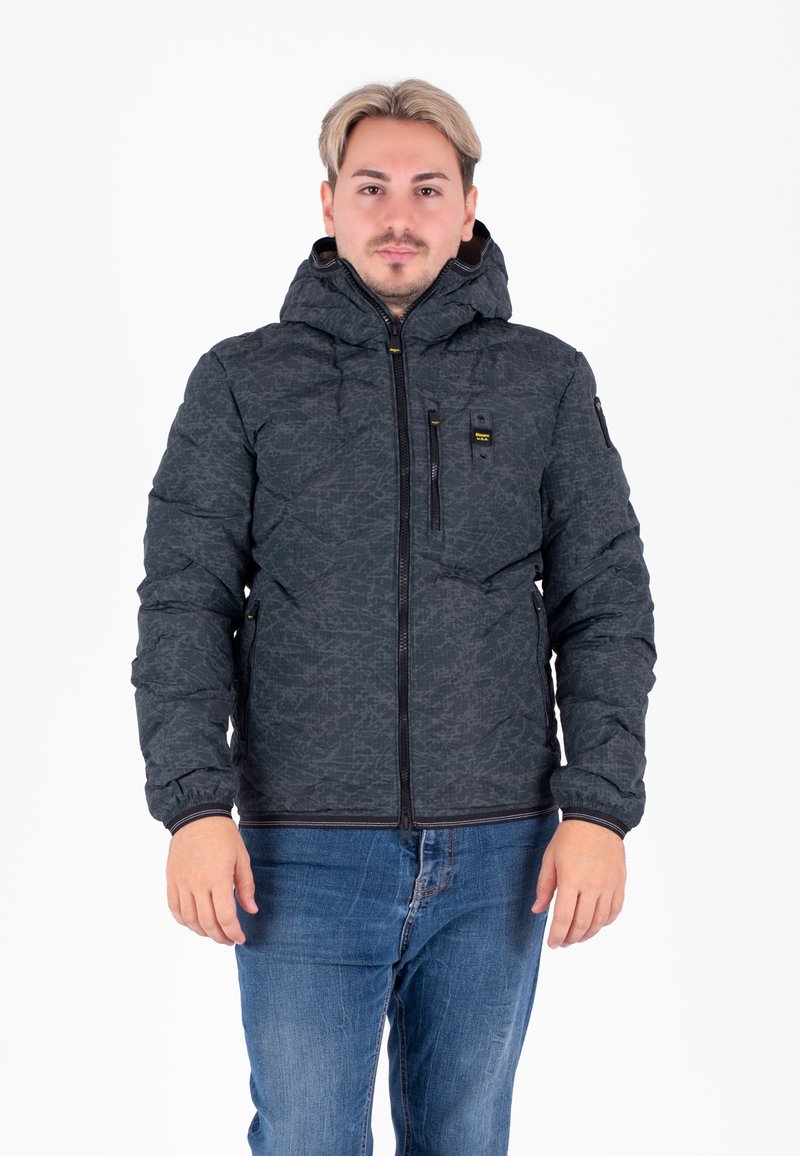 Giacca nera imbottita con un motivo testurizzato, cappuccio, chiusura con zip e tasche. Abbinata a jeans blu.