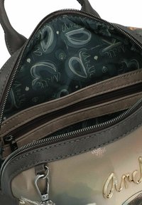 Sac à dos en simili cuir gris avec des accents métalliques, des poches zippées et un intérieur doté d'une doublure à motifs avec du texte et des formes.