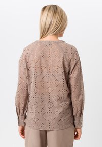 Lichtbruine blouse met ingewikkelde ruitvormige uitsparingen, lange mouwen en knoopmanchetten, gecombineerd met bijpassende broeken.