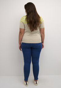 Beige top with short sleeves featuring neon green horizontal stripes, paired with blue skinny jeans and casual white sneakers.
