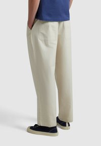 Beige weite Hosen aus strukturiertem Stoff mit zwei Gesäßtaschen. Kombiniert mit navy Sneakern mit hellen Sohlen.