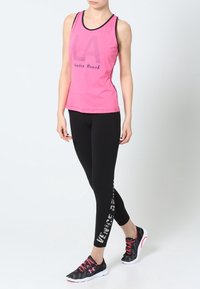 Lysrosa linne med texten "LA" och "Venice Beach", parat med svarta leggings med vit text och svarta träningsskor.