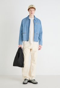 Jasnoniebieska dżinsowa kurtka z dwoma przednimi kieszeniami, noszona na beżowej koszuli, połączona z kremowymi spodniami i czarną pikowaną torbą. Szare buty dopełniają wygląd.