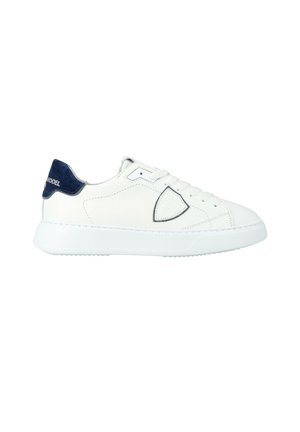 Baskets blanches basses avec un talon arrière bleu marine et une semelle en caoutchouc blanc arrondi, présentant un système de laçage et un logo discret cousu sur le côté.