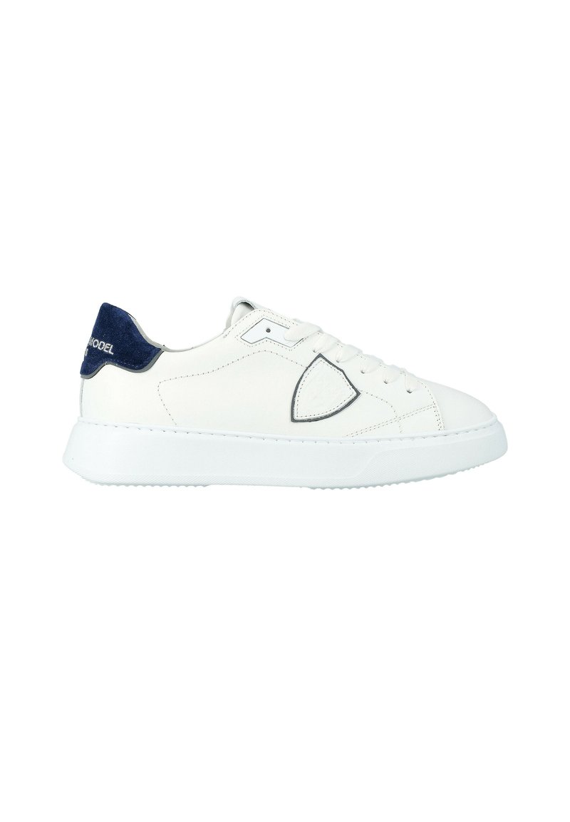 Witte low-top sneakers met een marineblauwe hieltab en een ronde witte rubberen zool, voorzien van vetersluiting en een subtiel geborduurd logo aan de zijkant.