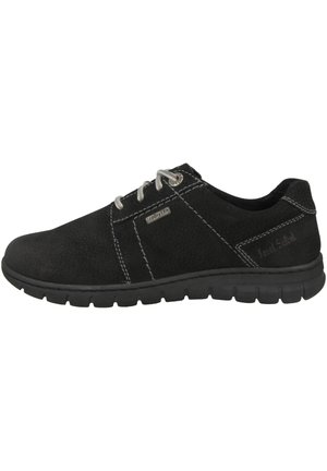 Black suede shoe with white stitching, lace-up front, textured design, and rubber sole; features metal accents and logo detail.