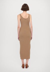 Beige ribattu lopputuulis midi-mekko, jossa on kaarrellinen selkäosa, esittelee kapeaa muotoa ja sivuaukkoja, yhdistettynä ruskeisiin blokkikorkoisiin kenkiin.