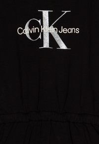 T-shirt preta em algodão com branding em glitter prateado "Calvin Klein Jeans", com detalhes plissados na cintura.