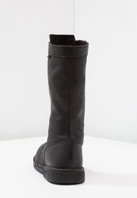 Botte en cuir noir avec un tige droite, surface texturée, accents de couture et une semelle plate. Aucun élément en métal ou décoratif visible.