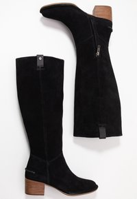 Black suede knee-high boots with stacked brown heels, side zipper, and pull tab, shown from side and top view on white background.