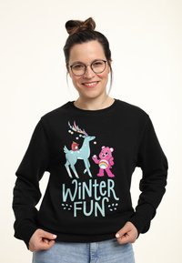 Zwarte sweatshirt met een grafisch ontwerp met kleurrijke cartoonfiguren: een teal rendier en een roze beer, tekst "WINTER FUN" in lichtblauw.