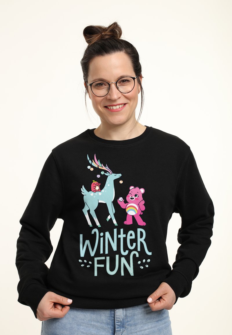Zwarte sweatshirt met een grafisch ontwerp met kleurrijke cartoonfiguren: een teal rendier en een roze beer, tekst "WINTER FUN" in lichtblauw.