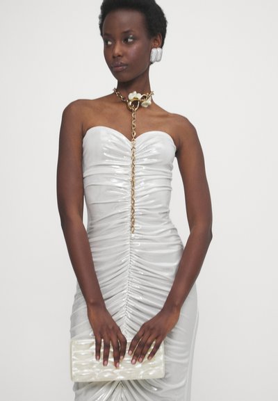 Trägerloses Silberkleid mit Raffungen, verziert mit einer goldenen Kette und einem floralen Akzent. Das Model hält eine strukturierte weiße Clutch. Glattes, glänzendes Material.