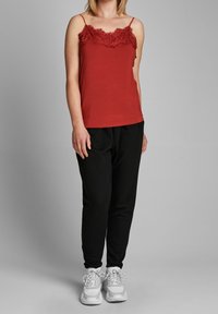 Canottiera rossa con bordo in pizzo sul collo, abbinata a pantaloni neri e sneaker bianche. Il tessuto è liscio; il design è leggero e casual.