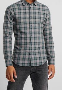 Grijs geruit shirt met een patroon van groene en rode lijnen, met een button-down kraag en lange mouwen. Gemaakt van een zachte, gestructureerde stof.