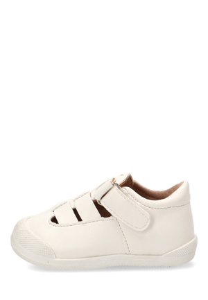 Sandalia blanca infantil de puntera cerrada con tira de velcro y suela de goma, vista lateral, mostrando diseño recortado para ventilación.