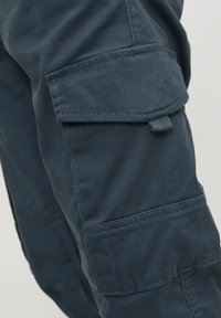 Mörkblå cargo-byxor med en texturerad tyg, sidofickor med lock och förstärkt sömnad längs sömmarna.