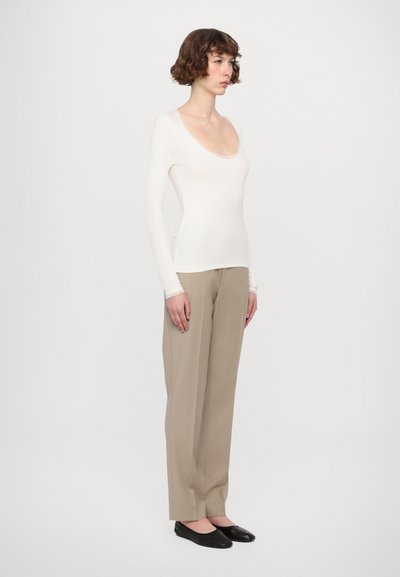 Long-sleeve, scoop-neck top in white fabric, paired with light beige, wide-leg trousers. Black flats complete the outfit.