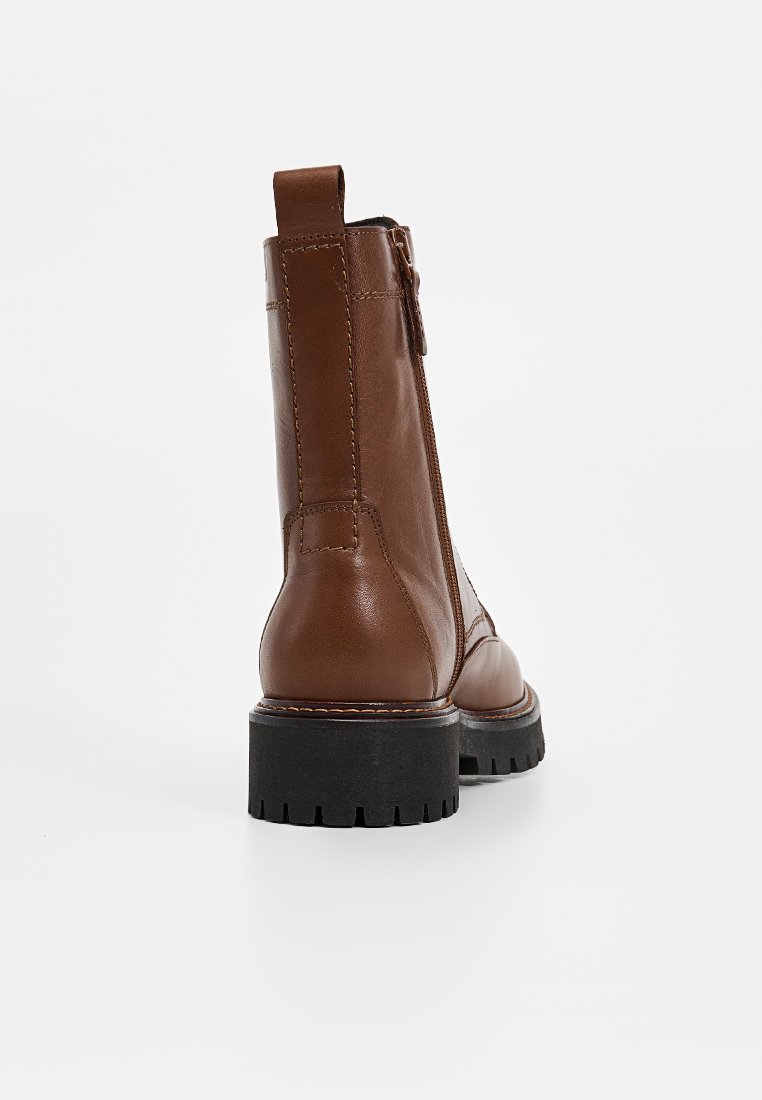 Braune Leder-Stiefelette mit strukturiertem Finish, strapazierfähiger schwarzer Gummisohle, rückseitiger Ziehschlaufe und sichtbarem Seitenreißverschluss.