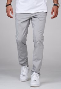 Ljust grå bomullbyxor med rak ben design, tillsammans med vita sneakers. Slät textur, rena linjer och inga synliga mönster eller detaljer.