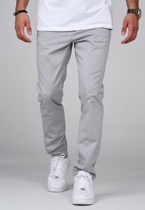 Ljust grå bomullbyxor med rak ben design, tillsammans med vita sneakers. Slät textur, rena linjer och inga synliga mönster eller detaljer.