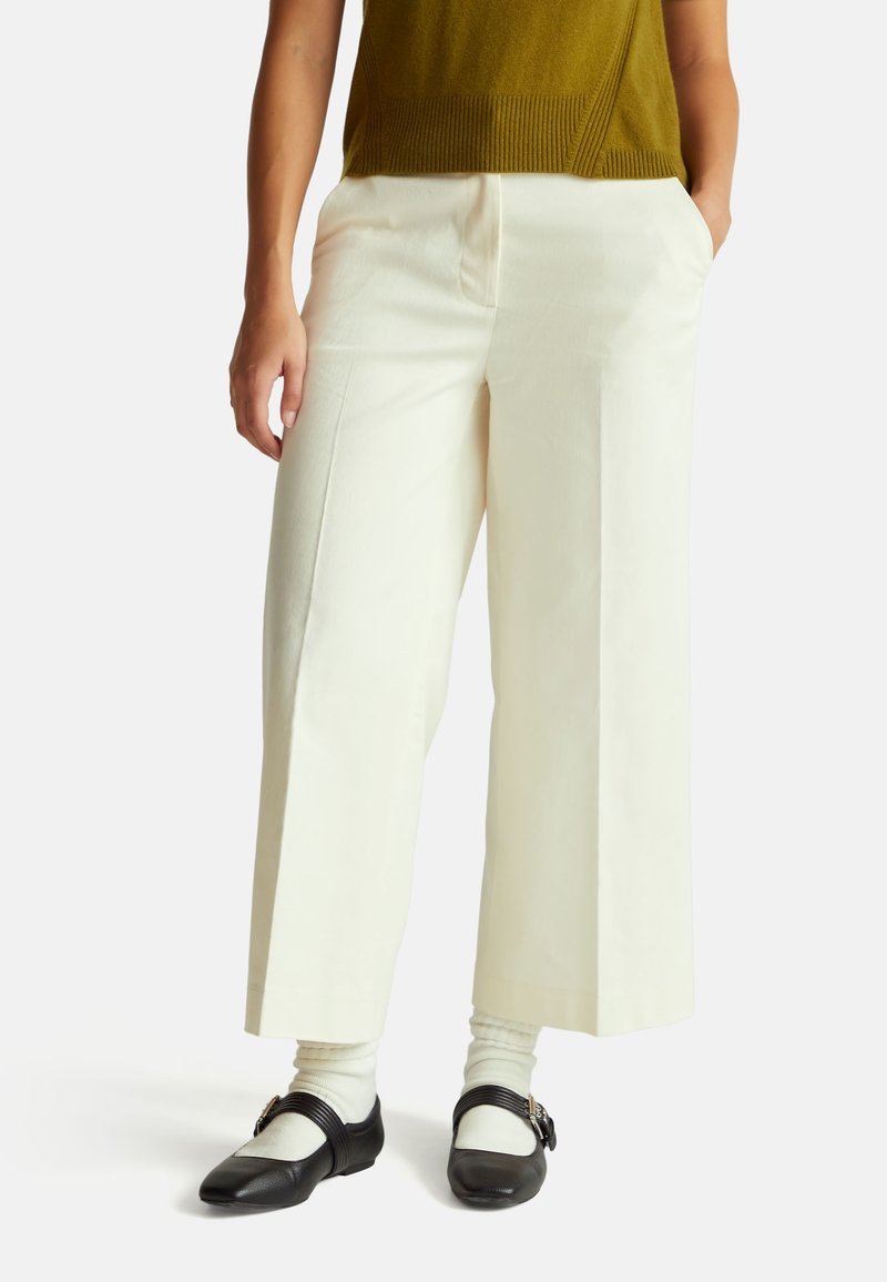 Wijd uitlopende, witte katoenen broeken met frontzakken. Gestyled met een donker olijfgroene gebreide top en zwarte Mary Jane schoenen met een band en gesp.