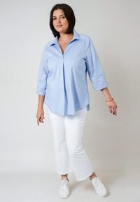 Chemise collerette bleu clair à manches longues avec un pli sur le devant, portée avec un jean blanc raccourci et des baskets blanches. Texture lisse et coupe décontractée.
