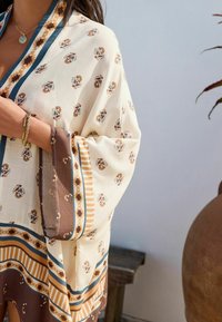 Kimono léger et à motifs en crème avec des détails floraux. Présente des rayures brunes et des accents bleus le long des bords. Tissu doux et fluide.