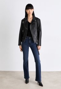 Svart skinnbikerjakke med glidelåslommer, kombinert med mørkeblå vide jeans og svarte hæler. Ensfarget, minimalistisk design.