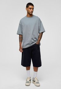 Lichtgrijze oversized t-shirt van zacht materiaal, gecombineerd met marineblauwe shorts, witte sokken en crèmekleurige sneakers met gaasaccenten.