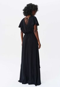 Robe maxi noire avec des manches flottantes, un dos en V, une taille élastique et des détails texturés le long de l'encolure. Tissu lisse et fluide.