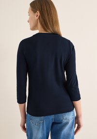 Haut bleu marine à manches longues avec une texture côtelée, un col rond et une coupe ajustée. Porté avec un jean en denim bleu clair.